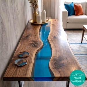 Könnte beinhalten: Ein Esstisch aus Walnussholz mit natürlicher Baumkante und einem zentralen Flussdesign aus durchscheinendem blauem Epoxidharz. Die Tischoberfläche ist glatt und poliert und zeigt natürliche Holzmaserungen. Zwei passende runde Untersetzer liegen darauf.
