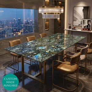Peut inclure: Une table à manger rectangulaire avec un plateau en pierre de labradorite bleue et verte polie et un cadre en métal doré, accompagnée de six chaises à cadre doré avec des sièges en cuir beige. Un lustre en cristal à étages est suspendu.