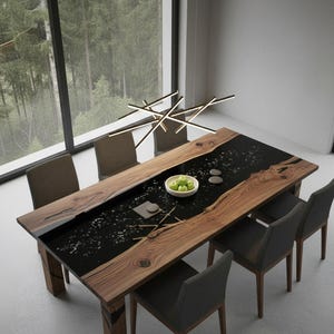 Puede incluir: Una mesa de comedor moderna de madera con un centro de resina epoxi negra. La mesa está rodeada por seis sillas grises tapizadas. Un cuenco con manzanas verdes y piedras decorativas está sobre la mesa. Una moderna lámpara cuelga sobre la mesa.
