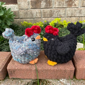 May include: Two crocheted plush chickens, one gray with blue accents and one black, both with red velvet combs and yellow feet.