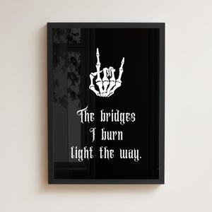 Könnte beinhalten: Gerahmter Kunstdruck mit einer weißen Skelett-Handgeste und gotischem Text auf schwarzem Hintergrund. Der Text lautet: "The bridges I burn light the way."