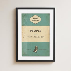 May include: A framed print featuring a teal and cream book cover design with the text FIRST EDITION, PEOPLE, WHAT A TERRIBLE IDEA, COMPLETE, and UNABRIDGED. A small illustration of a puffin is centered at the bottom of the rectangular artwork.