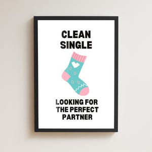 Pode incluir: Uma impressão emoldurada com as palavras "CLEAN SINGLE" acima de uma meia azul-turquesa com detalhes rosa e um coração branco. Abaixo da meia, o texto diz "LOOKING FOR THE PERFECT PARTNER". A impressão está em uma moldura preta.