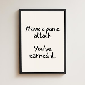 May include: A framed print with a black border. The print has a cream-colored background with black handwritten text that reads: "Have a panic attack. You've earned it."