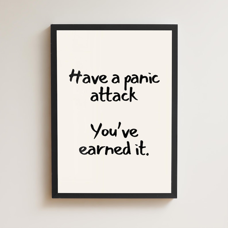 May include: A framed print with a black border. The print has a cream-colored background with black handwritten text that reads: "Have a panic attack. You've earned it."