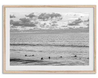 Può includere: Stampa incorniciata in bianco e nero di surfisti nell'oceano. L'immagine mostra diversi surfisti in acqua, con un cielo nuvoloso e l'orizzonte sullo sfondo. La cornice è in legno chiaro.