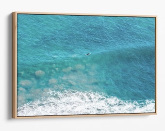 Könnte beinhalten: Eine Luftaufnahme eines Surfers, der auf einem Surfbrett in einem türkisfarbenen Meer paddelt, mit weißen, schaumigen Wellen, die an der Küste brechen.