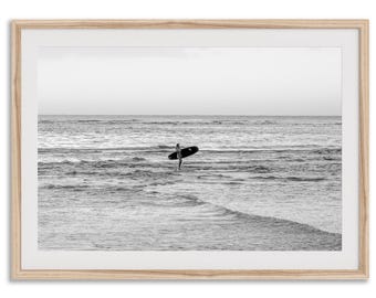 Könnte beinhalten: Schwarz-Weiß-Druck in einem Rahmen eines Surfers im Meer mit einem Surfbrett. Der Surfer befindet sich in der Mitte des Bildes, mit dem Meer und dem Himmel im Hintergrund. Der Druck ist in einem hellen Holzrahmen.