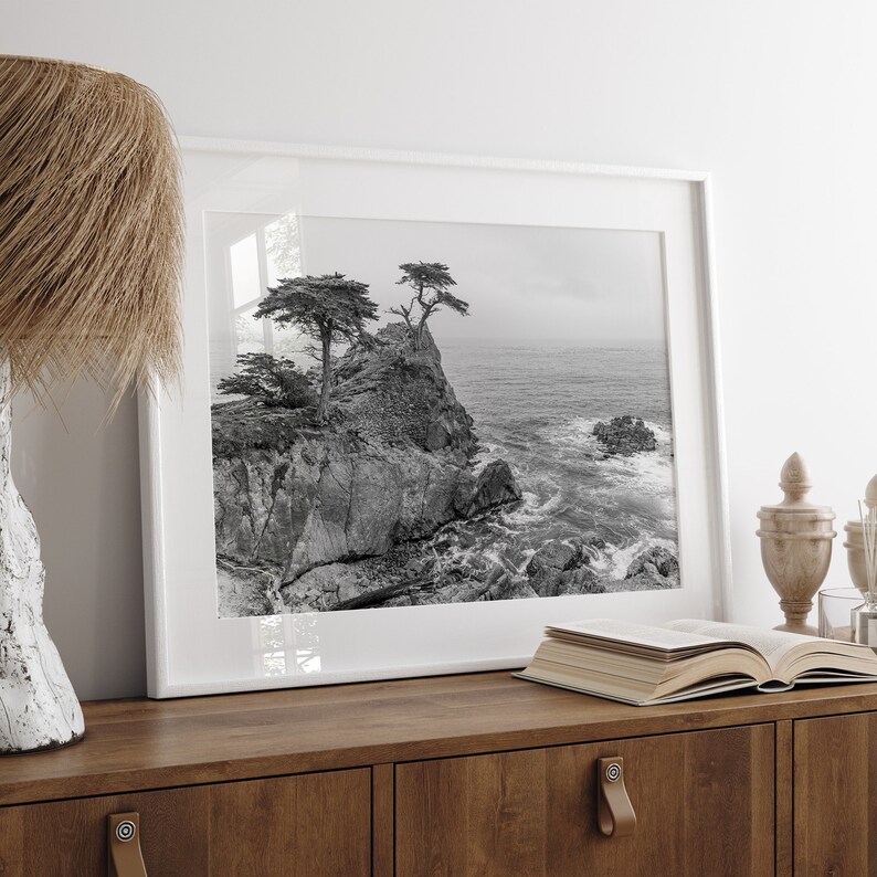 Black and white photo of Lone Cypress on a cliffside along 17-Mile Drive near Monterey, California, with waves crashing against rocks below.