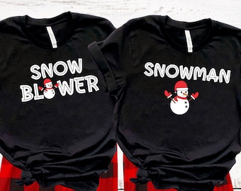 Puede incluir: Dos camisetas negras con un diseño de muñeco de nieve. Una camiseta dice "Snow Blower" con un gráfico de muñeco de nieve. La otra camiseta dice "Snowman" con un gráfico de muñeco de nieve. Las camisetas se llevan sobre pantalones de pijama de cuadros rojos y negros.