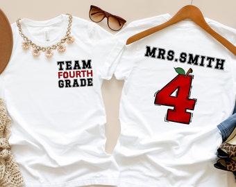 Könnte beinhalten: Zwei weiße T-Shirts, eines mit dem Text "TEAM FOURTH GRADE" und das andere mit dem Text "MRS. SMITH" und einem roten Apfel mit der Zahl "4" darin.