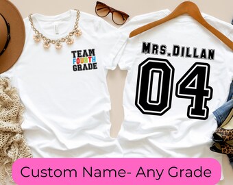 May include: Two white t-shirts with custom text. One says "TEAM FOURTH GRADE" in black, red, blue, and white. The other displays "MRS. DILLAN" and the number "04" in black. A pink banner at the bottom says "Custom Name- Any Grade".