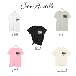 K&ouml;nnte beinhalten: F&uuml;nf T-Shirts in verschiedenen Farben mit dem Aufdruck "TEAM THIRD" auf der Vorderseite. Die Farben sind wei&szlig;, grau, schwarz, rosa und natur.