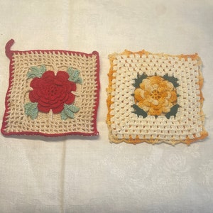 May include: Two crocheted pot holders with floral designs. One is cream with a red rose and green leaves. The other is cream with a yellow flower and green leaves.
