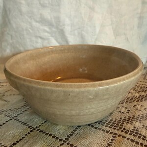 May include: A tan ceramic mixing bowl with a wide rim. The bowl has a smooth, slightly glossy finish and a simple, classic design. The bowl is likely used for food preparation.