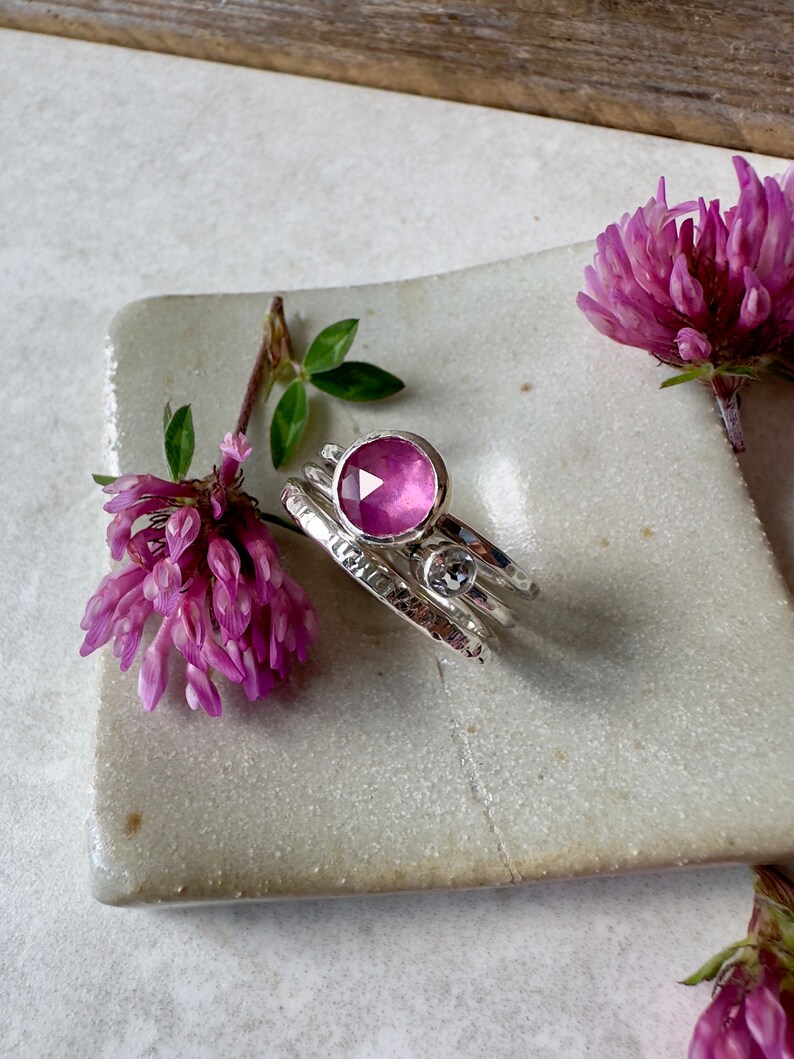 K&ouml;nnte beinhalten: Ein Set aus drei Silberringen mit einem rosafarbenen Edelstein in der Mitte. Die Ringe sind texturiert und haben eine geh&auml;mmerte Oberfl&auml;che. Der Edelstein ist rund und facettiert.