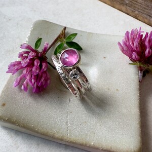 K&ouml;nnte beinhalten: Drei &uuml;bereinander gestapelte Silberringe, der oberste Ring hat einen rosafarbenen Edelstein, der mittlere Ring einen kleineren, klaren Edelstein und der unterste Ring ist ein schlichtes Band.