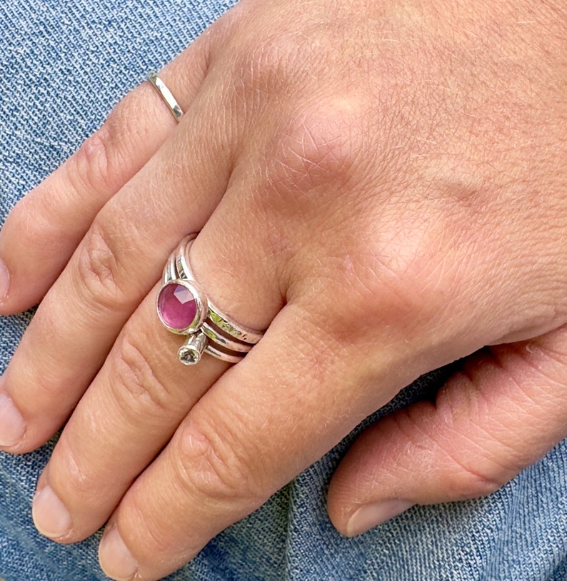 K&ouml;nnte beinhalten: Ein silberner Ring mit einem rosafarbenen Stein in der Mitte. Der Ring ist mit zwei weiteren silbernen B&auml;ndern &uuml;bereinander gelegt.