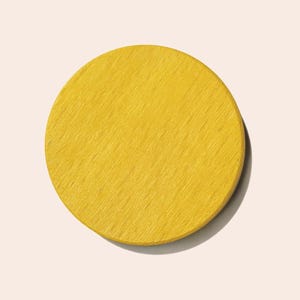 May include: A solid yellow, circular wooden coaster. The coaster has a visible wood grain texture and is set against a light pink background. The coaster is a simple, minimalist design.