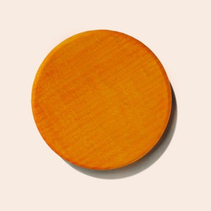 May include: A round, orange wooden disc with a smooth, slightly textured surface.