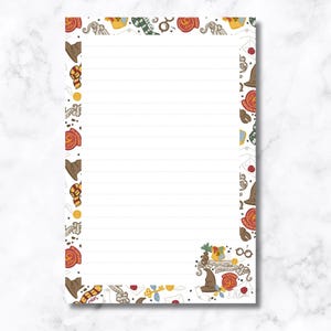 May include: White lined stationery paper with a decorative border featuring illustrations of a sorting hat, scarves, and other magical elements. The stationery is designed with a theme of fantasy and magic.