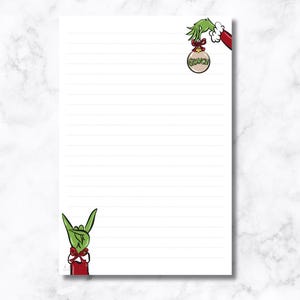 May include: White lined notepad with Grinch-themed illustrations. Features a green hand holding a Christmas ornament with "Grinch" text and a green hand making a rock-and-roll gesture. Red and white accents add a festive touch.