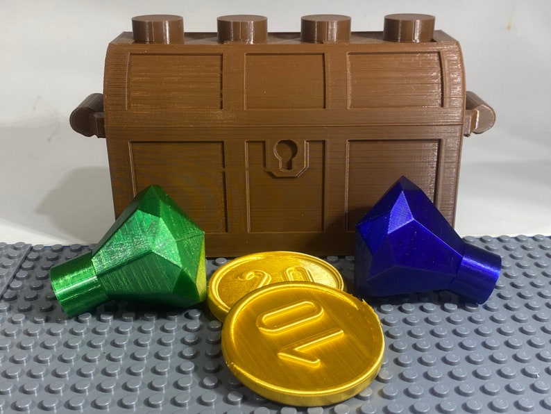 May include: A brown wooden treasure chest with a gold keyhole, open to reveal two gems: a green one and a blue one.  There are also two gold coins with the number "20" on them.