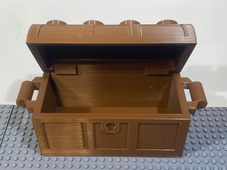 May include: A brown wooden treasure chest with a hinged lid and two handles. The chest is open and empty.