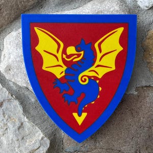 May include: A shield-shaped emblem with a blue border, red center, and a yellow dragon design. The dragon is blue with yellow wings. The shield is likely a decorative item or a collectible.