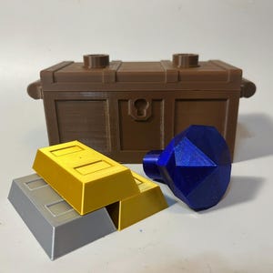 May include: A brown wooden treasure chest with a keyhole, two gold bars, and a blue gemstone.