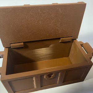 May include: A brown wooden treasure chest with a hinged lid and two handles. The chest is open and empty.