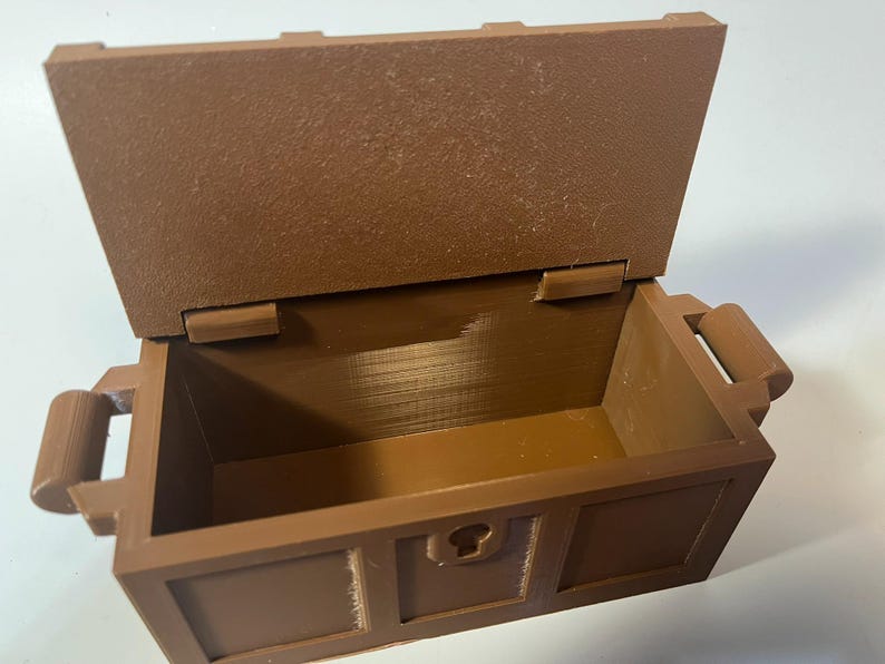 May include: A brown wooden treasure chest with a hinged lid and two handles. The chest is open and empty.
