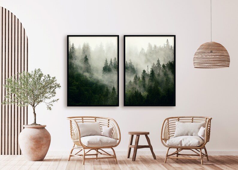 May include: Two framed prints of a misty forest scene with tall trees. The prints are hung on a white wall in a living room setting with two wicker chairs and a small wooden stool.