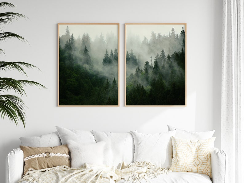 May include: Two framed prints of a misty forest scene with tall evergreen trees. The prints are in a light wood frame and are hung on a white wall.