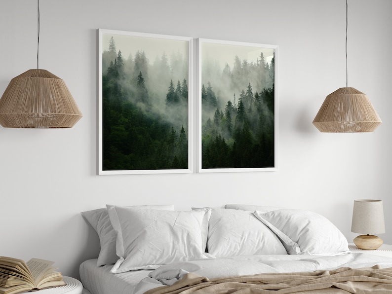 May include: Two framed prints of a misty forest scene with tall green trees. The prints are hung on a white wall above a bed with white bedding.
