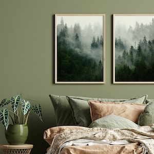 May include: Two framed prints of a misty forest scene with tall green trees. The prints are hanging on a sage green wall above a bed with a brown and green linen bedding set.