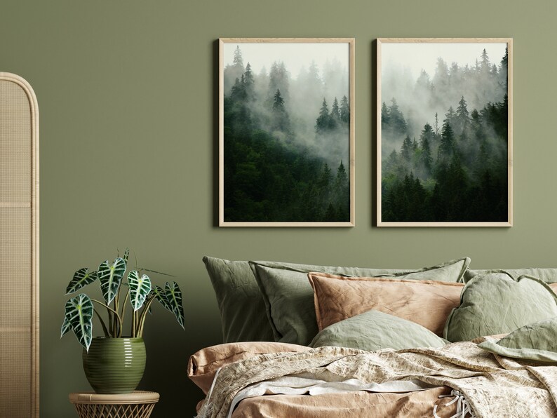 May include: Two framed prints of a misty forest scene with tall green trees. The prints are hanging on a sage green wall above a bed with a brown and green linen bedding set.