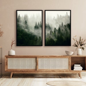 May include: Two framed black and white photographs of a misty forest scene. The photographs are hanging on a light brown wall above a wooden cabinet with a woven rattan front.