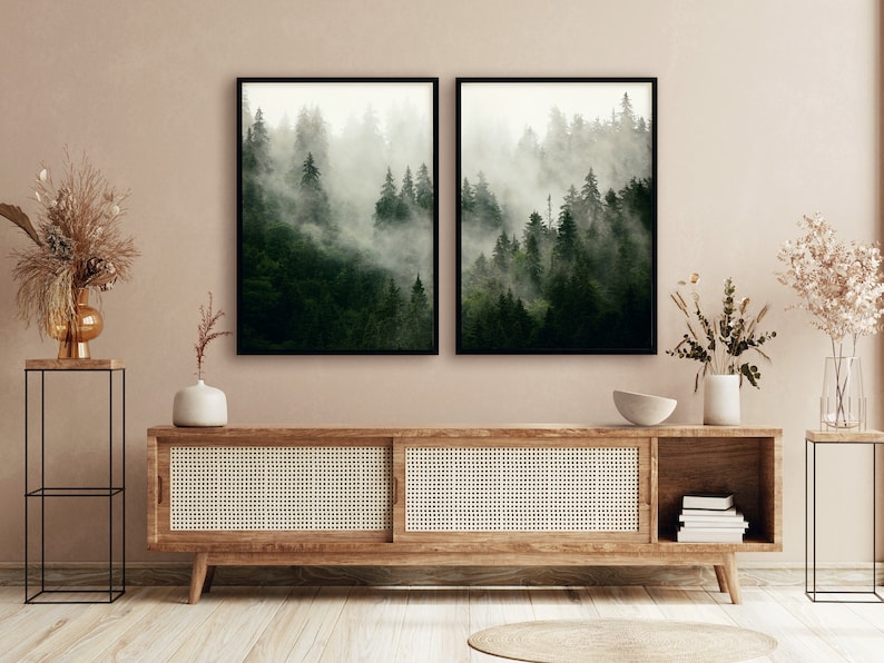 May include: Two framed black and white photographs of a misty forest scene. The photographs are hanging on a light brown wall above a wooden cabinet with a woven rattan front.