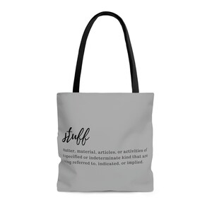 May include: A gray tote bag with black handles. The bag has the word "stuff" written in black cursive lettering, followed by a definition of the word in smaller black lettering.