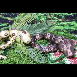 Puede incluir: Dos figuras de serpiente articuladas con cuerpos segmentados. Una serpiente es de color crema con manchas marrones y una cresta oscura, mientras que la otra es de color marrón oscuro con manchas más claras y una cresta a juego. Ambas tienen ojos grandes.