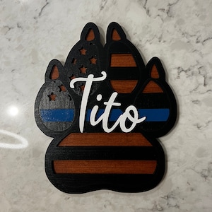May include: Black wooden paw print with a blue and white American flag, a blue and white police thin blue line, and the name "Tito" in white lettering.