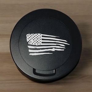 May include: A black round gas cap with a white distressed American flag design.