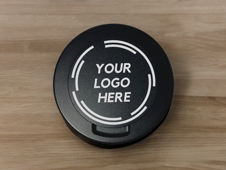 Op de afbeelding: Een rond zwart deksel met een witte cirkel en de tekst "YOUR LOGO HERE" in het midden.