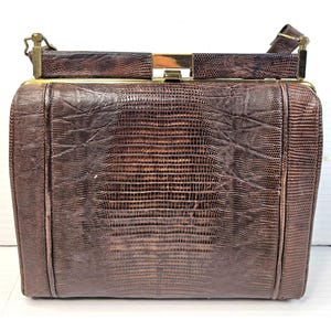 May include: A brown leather handbag with a gold clasp and a textured, snake-like pattern.