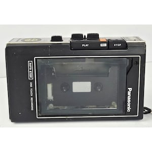 May include: A black Panasonic portable cassette recorder featuring a clear plastic tape compartment, top-mounted control buttons labelled PLAY, REC, and STOP, and white text on the front panel indicating AUTO STOP and ONE TOUCH RECORDING features.