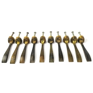 May include: A set of ten antique-style brass drawer pulls, each featuring a hinged, elongated drop handle attached to a small mounting base with a single protruding metal screw for installation, displaying a weathered, dark metallic patina.