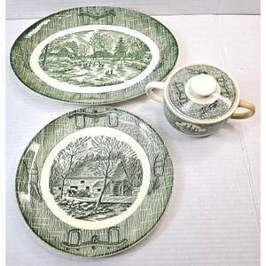 Puede incluir: Un juego de vajilla vintage verde y blanco que incluye una fuente ovalada, un plato redondo y un cuenco pequeño con tapa. Cada pieza presenta un diseño de paisaje rural en verde y blanco.