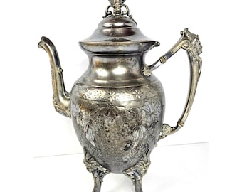 Tetera antigua chapada en plata, ornamentada, con grabados florales y diseño de patas de león.