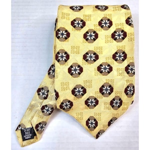May include: A yellow silk tie featuring a repeating pattern of octagonal shapes in burgundy, white, and brown. The tie is folded and has a label that reads "Custom of 100% Silk Imported Fabric."